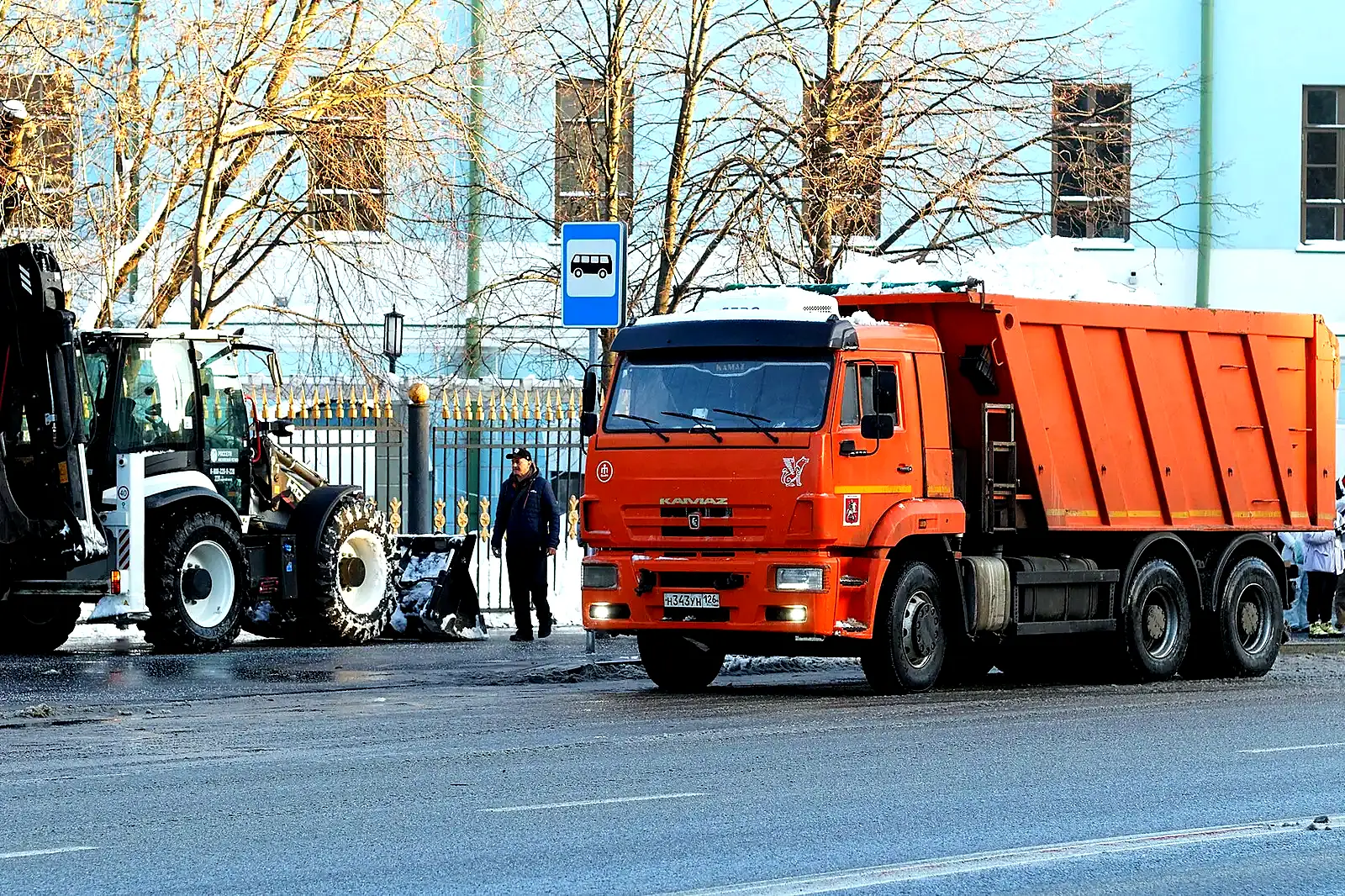Погрузчик и самосвалы на уборке снега в городе